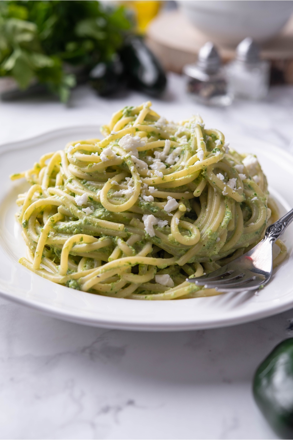 A bed of green spaghetti topped with Cotija on a white plate with a fork on the plate.