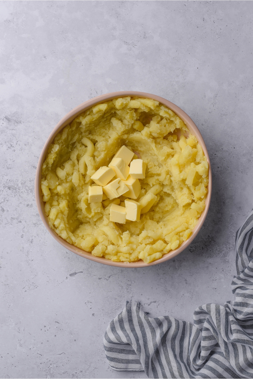 A bowl of mashed potatoes with a pile of cubed butter in the center of the bowl.