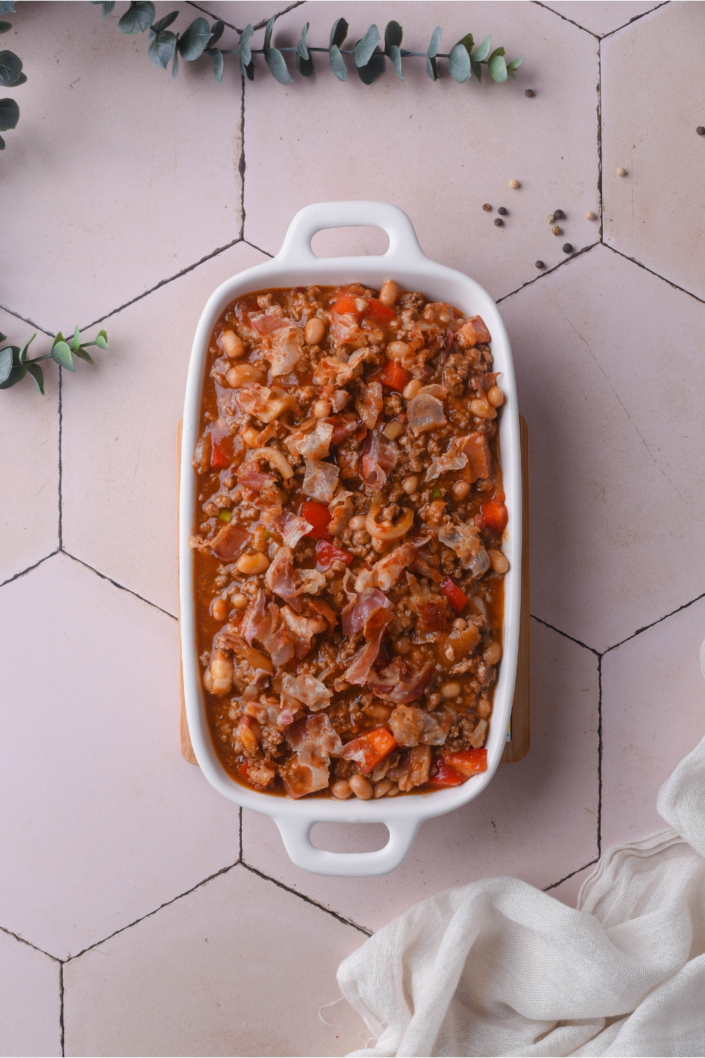 Overview of a white baking dish filled with baked beans with ground beef, bacon, diced peppers and diced onions.