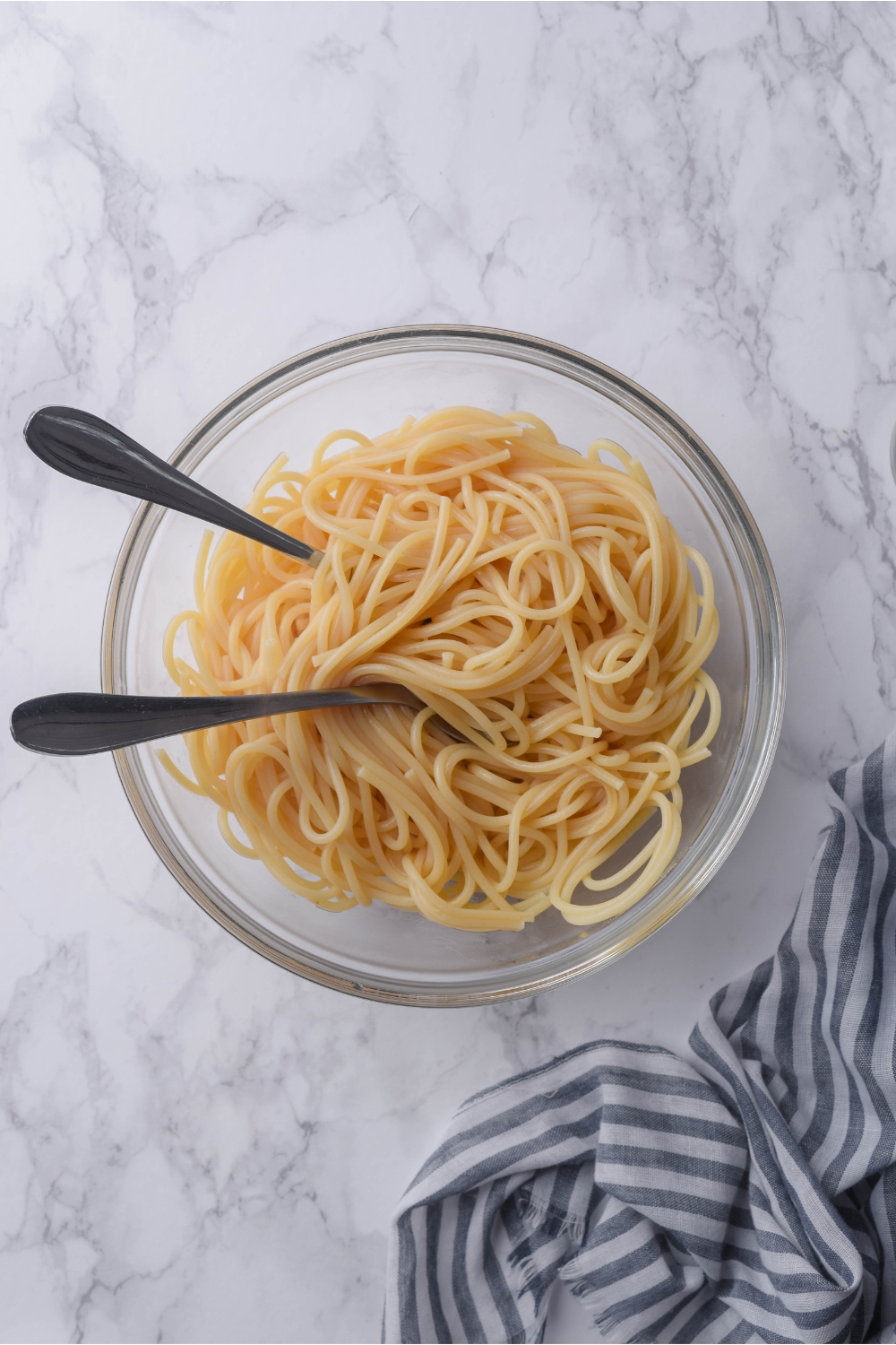 Cooked spaghetti noodles in a clear bowl with two forks in the bowl.