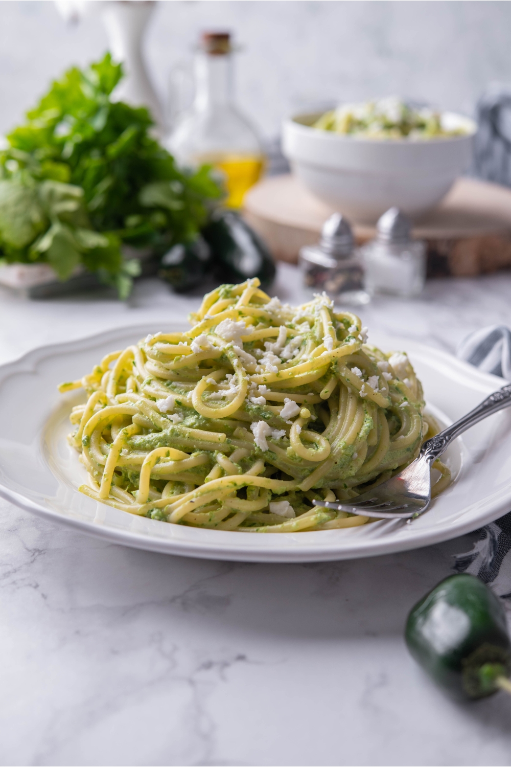 A bed of green spaghetti topped with Cotija on a white plate with a fork on the plate.