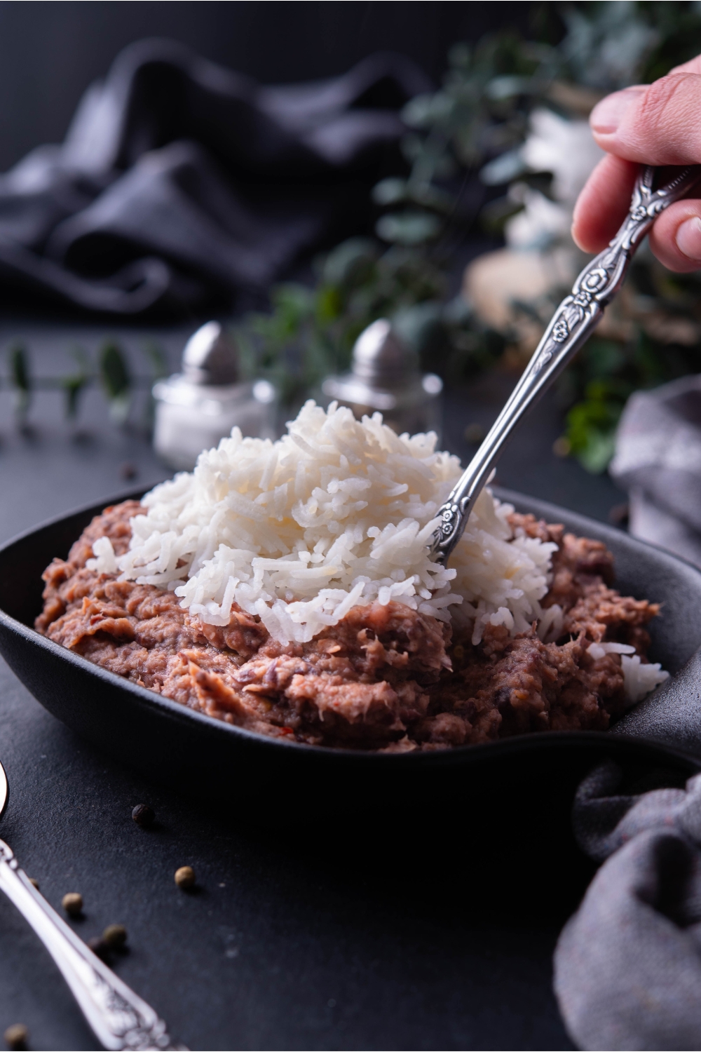 A hand scooping a bite of beans and rice with a fork from a black bowl filled with beans and rice.