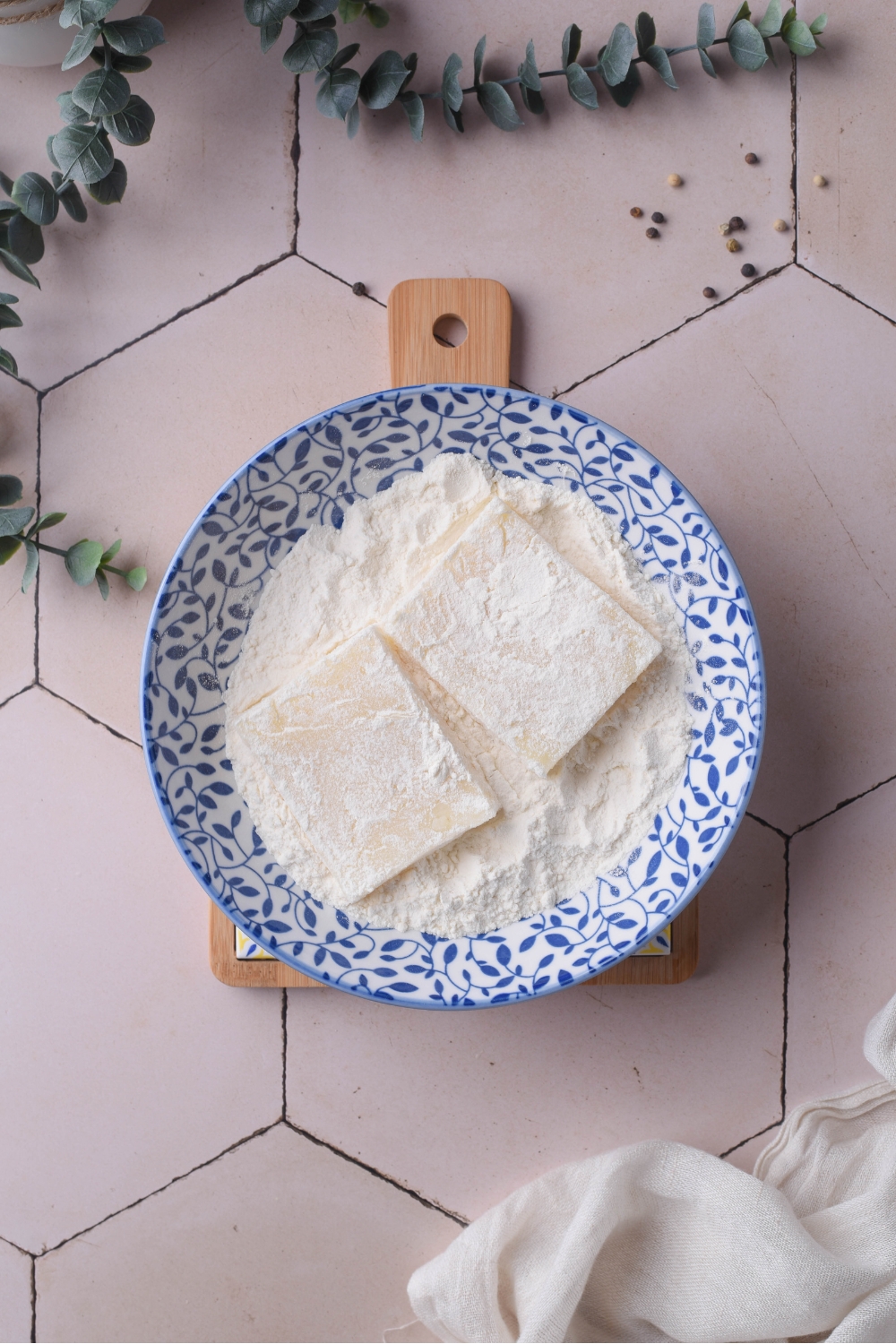 A blue and white shallow dish with two grit cakes coated in a flour mixture.