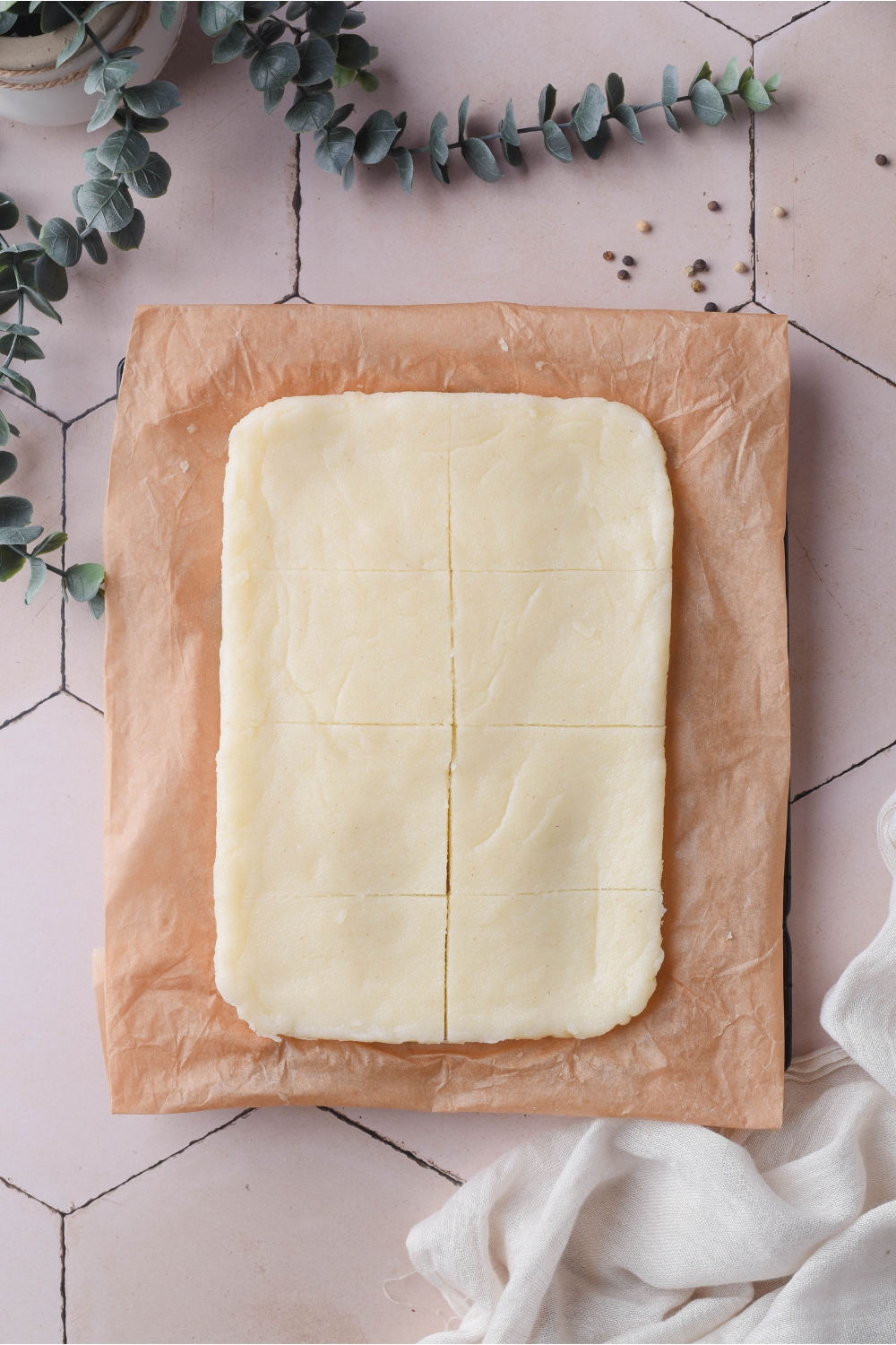 A rectangle of flattened, cooked grits laid out over a sheet of parchment paper. The grits have been cut into equal-sized squares.