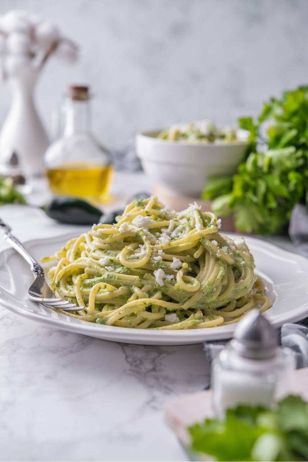 A bed of green spaghetti topped with Cotija on a white plate with a fork on the plate.