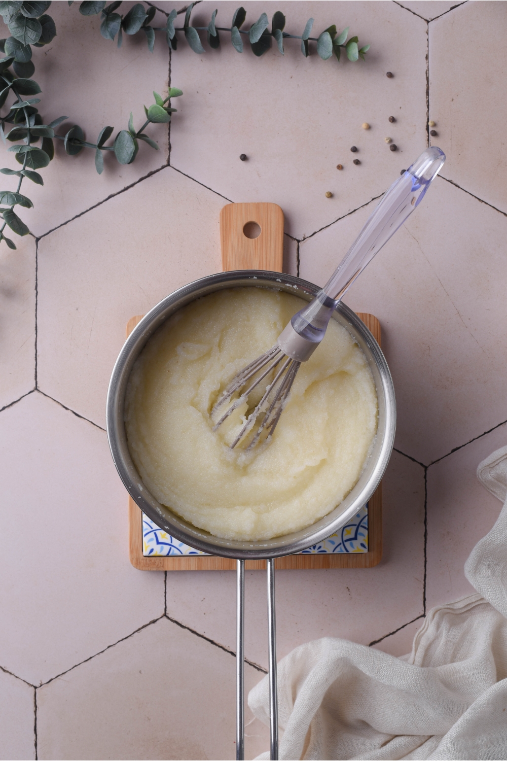 A pot filled with cooked grits and a whisk is in the pot.