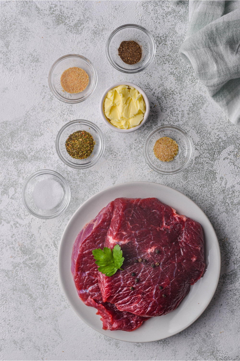 An assortment of ingredients including a plate of raw flat iron steak and bowls of spices and butter.