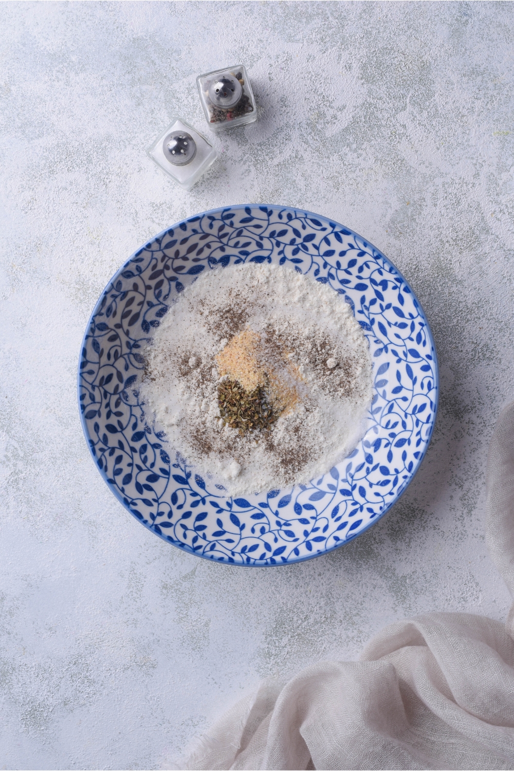 A white and blue decorative bowl with flour and a mixture of spices that have not been fully combined.