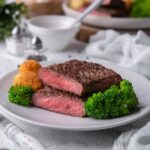 Flat iron steak cut in half with each half stacked on each other, on a white plate with broccoli and nuggets on the plate.