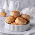 A white dish atop a white serving tray with a pile of Popeye's biscuits in the dish.
