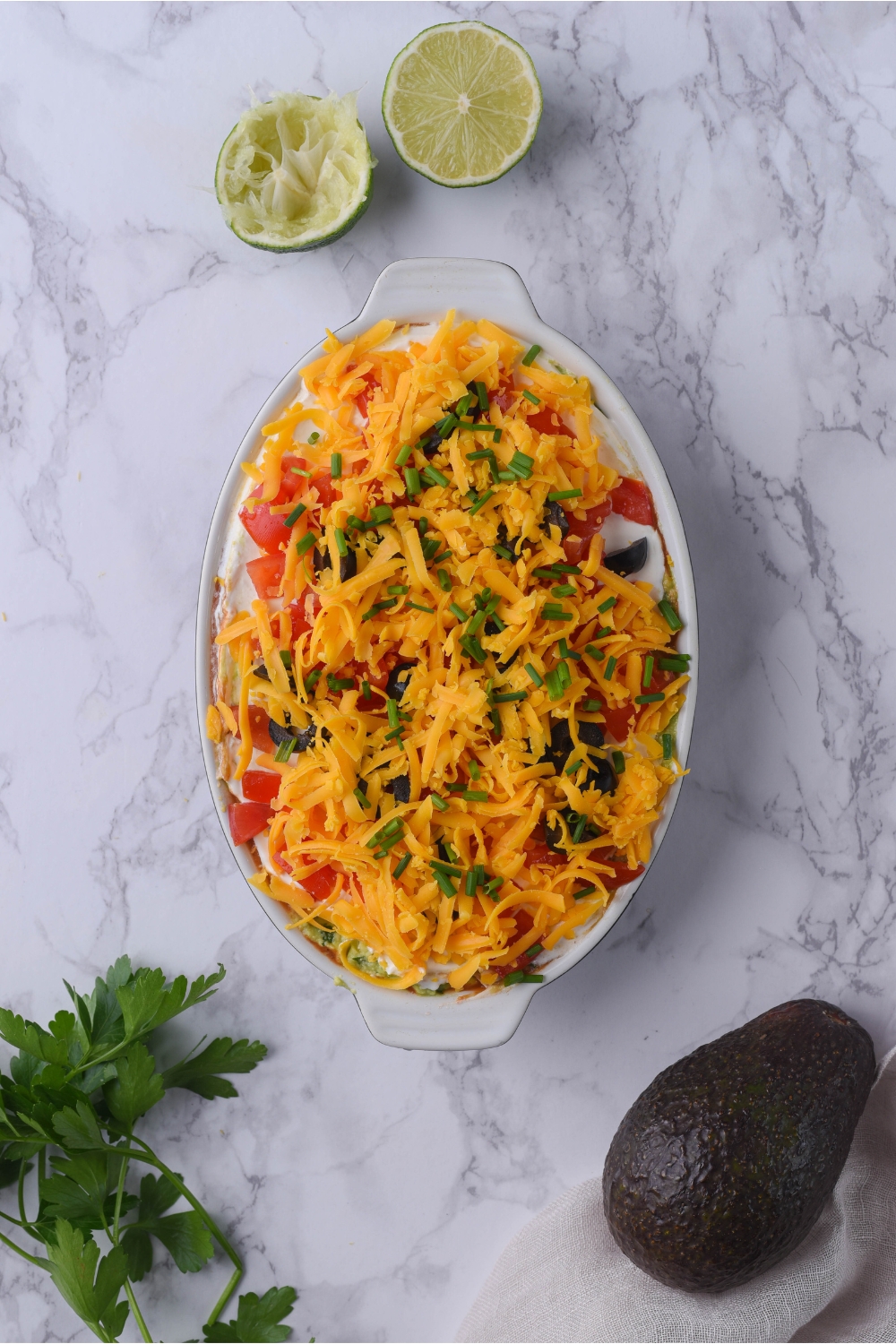 7 layer dip in a white baking dish topped with shredded cheese and fresh herbs.