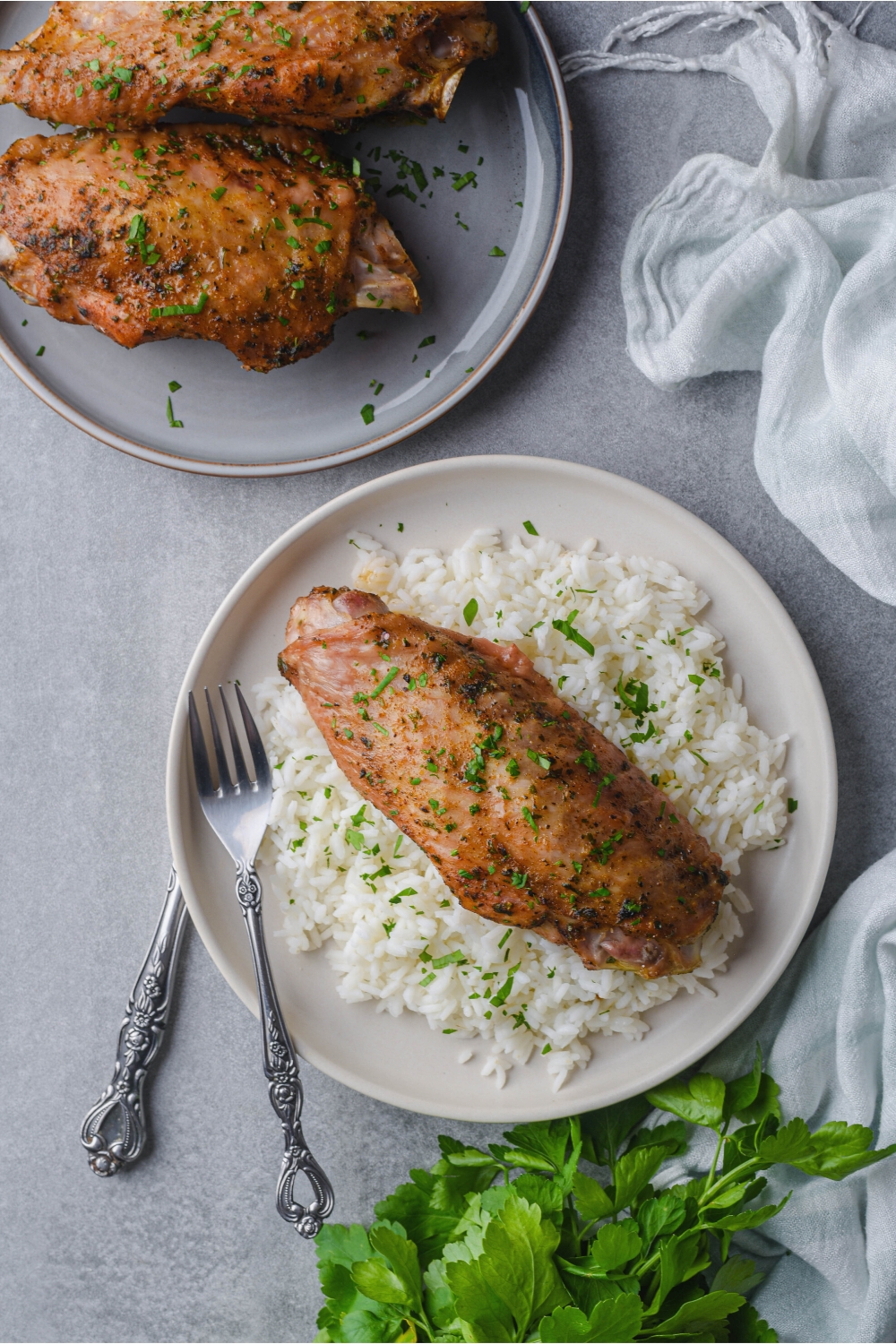 A turkey wing on top of white rice on top of a plate. Behind it is two more turkey wings on a plate.