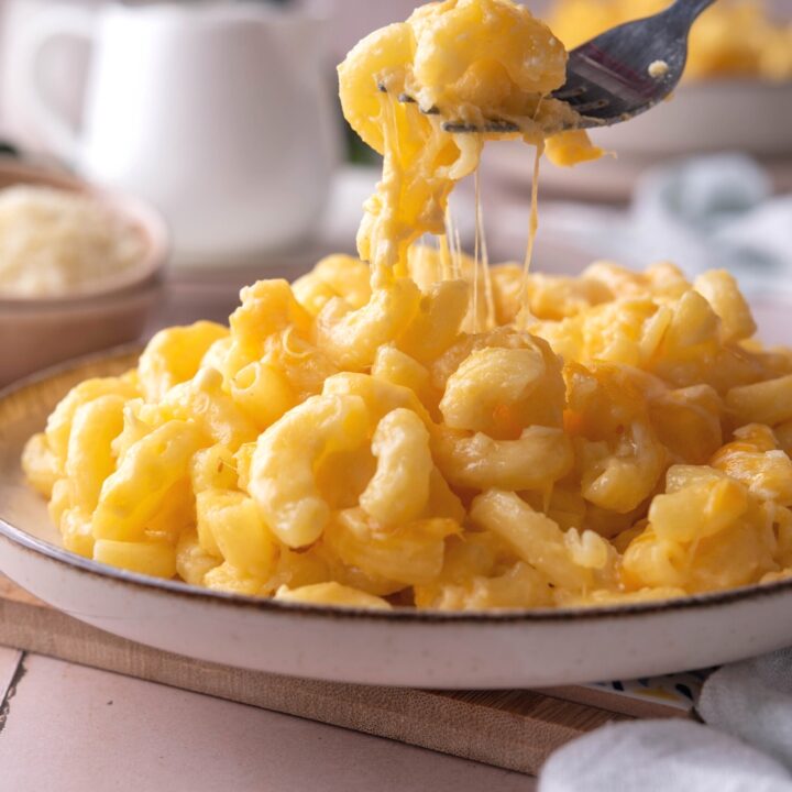 A fork scooping some mac and cheese from a plate that is filled with the mac and cheese.