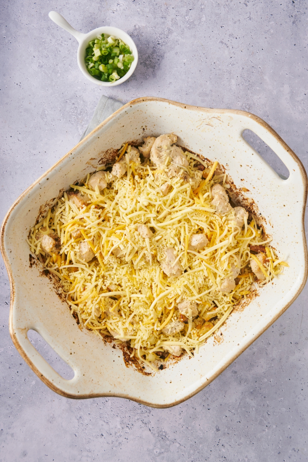 A casserole dish with potatoes, chicken and shredded cheese on top.