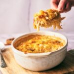 A spoon holding a large scoop of cheesy chicken and rice casserole over the baking dish as to serve it.
