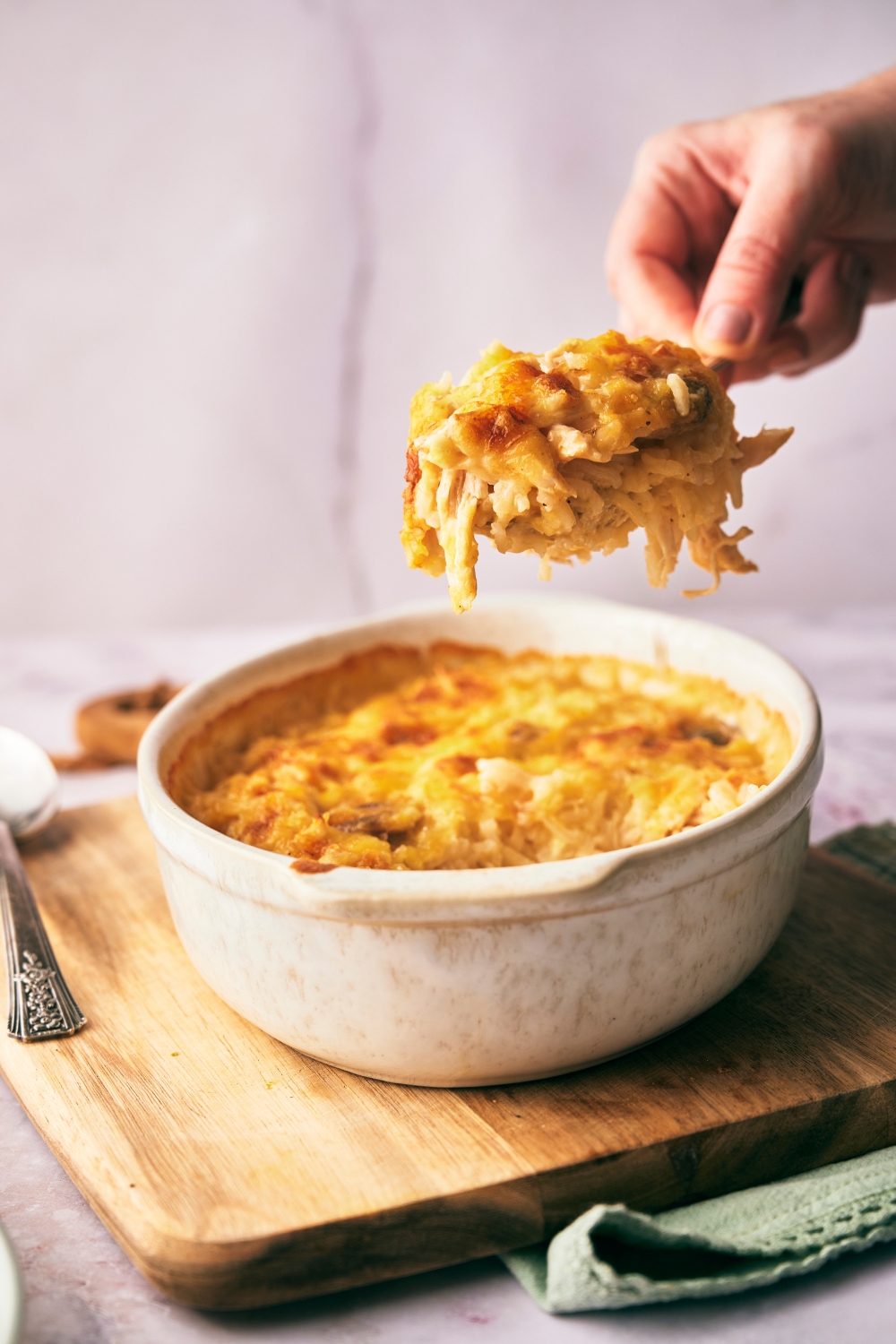 A spoon holding a large scoop of cheesy chicken and rice casserole over the baking dish as to serve it.