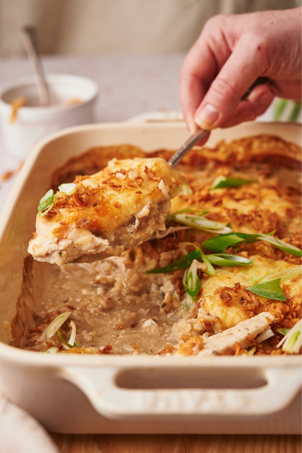 A casserole dish with a spoon serving a serving of chicken casserole out of the casserole dish.