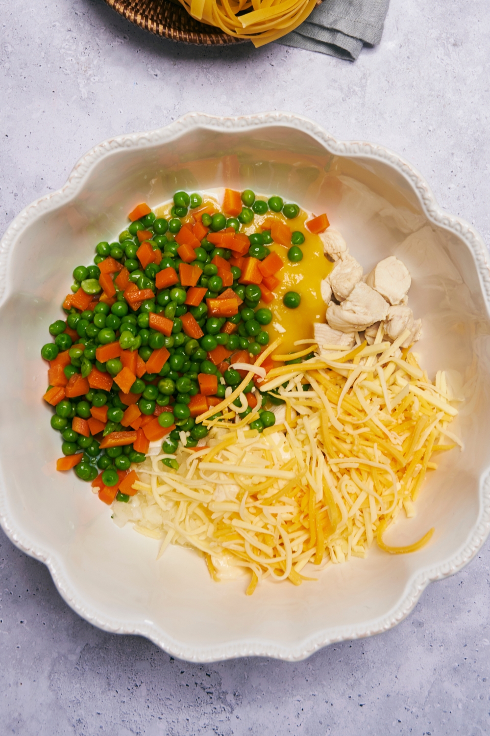 A mixing bowl with frozen peas and carrots, shredded cheese, cream of chicken soup, and chopped cooked chicken.