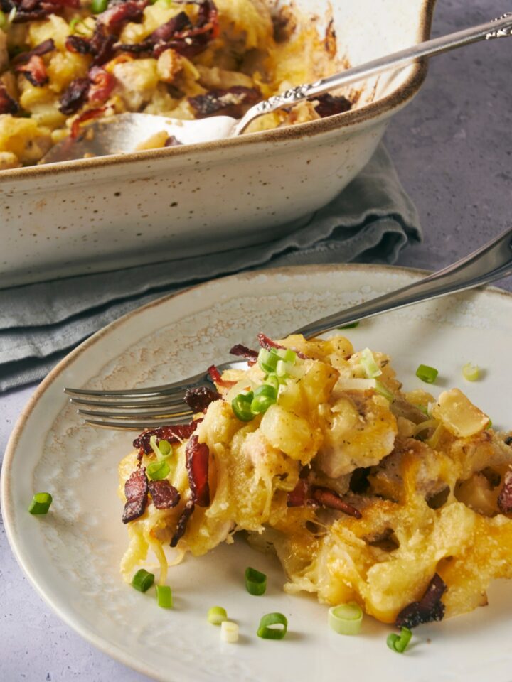 A serving plate with a serving of chicken potato casserole. A casserole dish with the remaining chicken potato casserole is next to the plate.