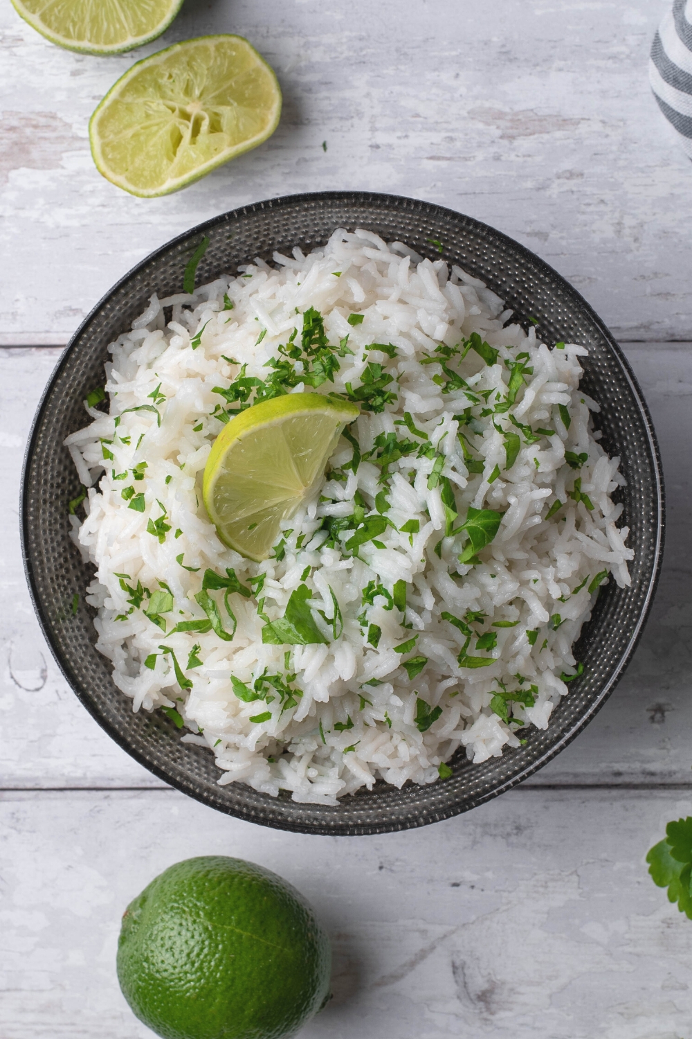 A lime and chopped cilantro on top white rice in a bowl.