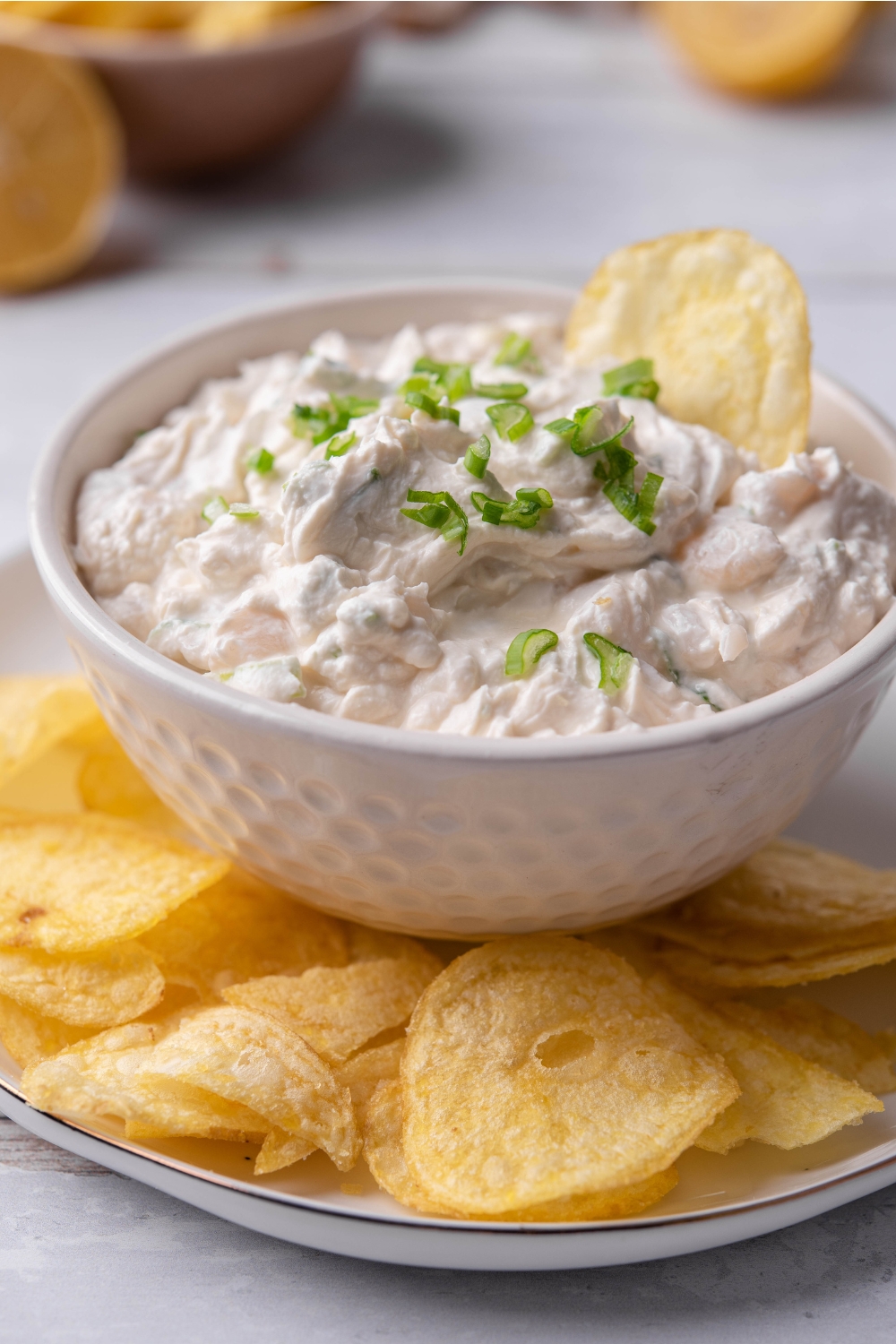 A small dip dish with clam dip in it being served on a plate with potato chips.