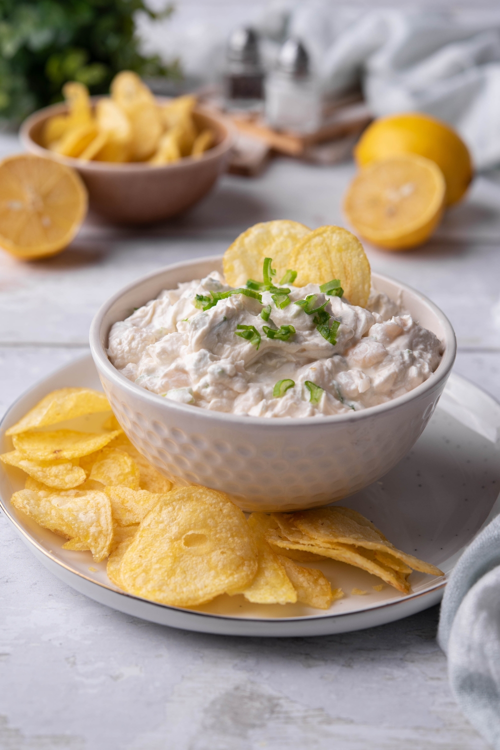 A small dip dish with clam dip in it being served on a plate with potato chips.