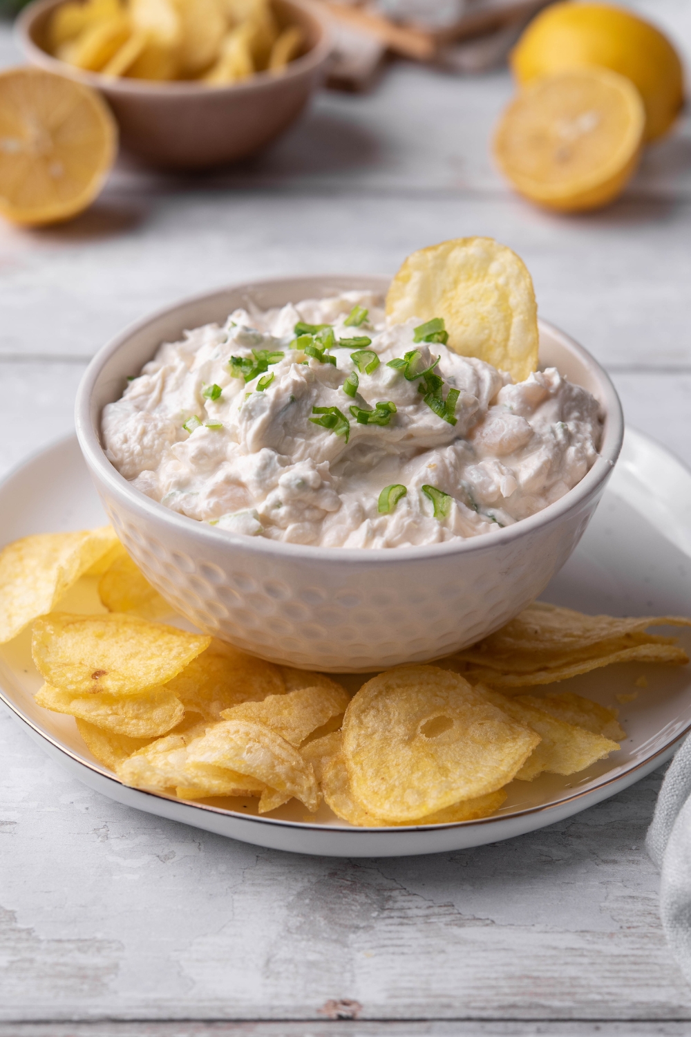 A small dip dish with clam dip in it being served on a plate with potato chips.\