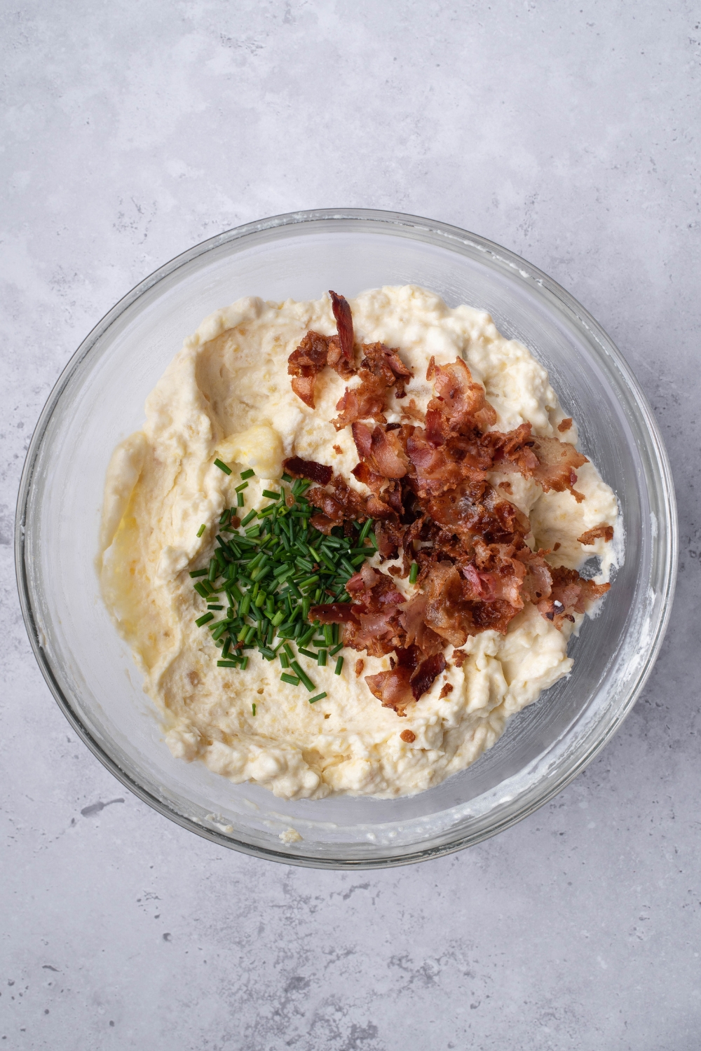 A mixing bowl with mashed potatoes, chives, and bacon bits.