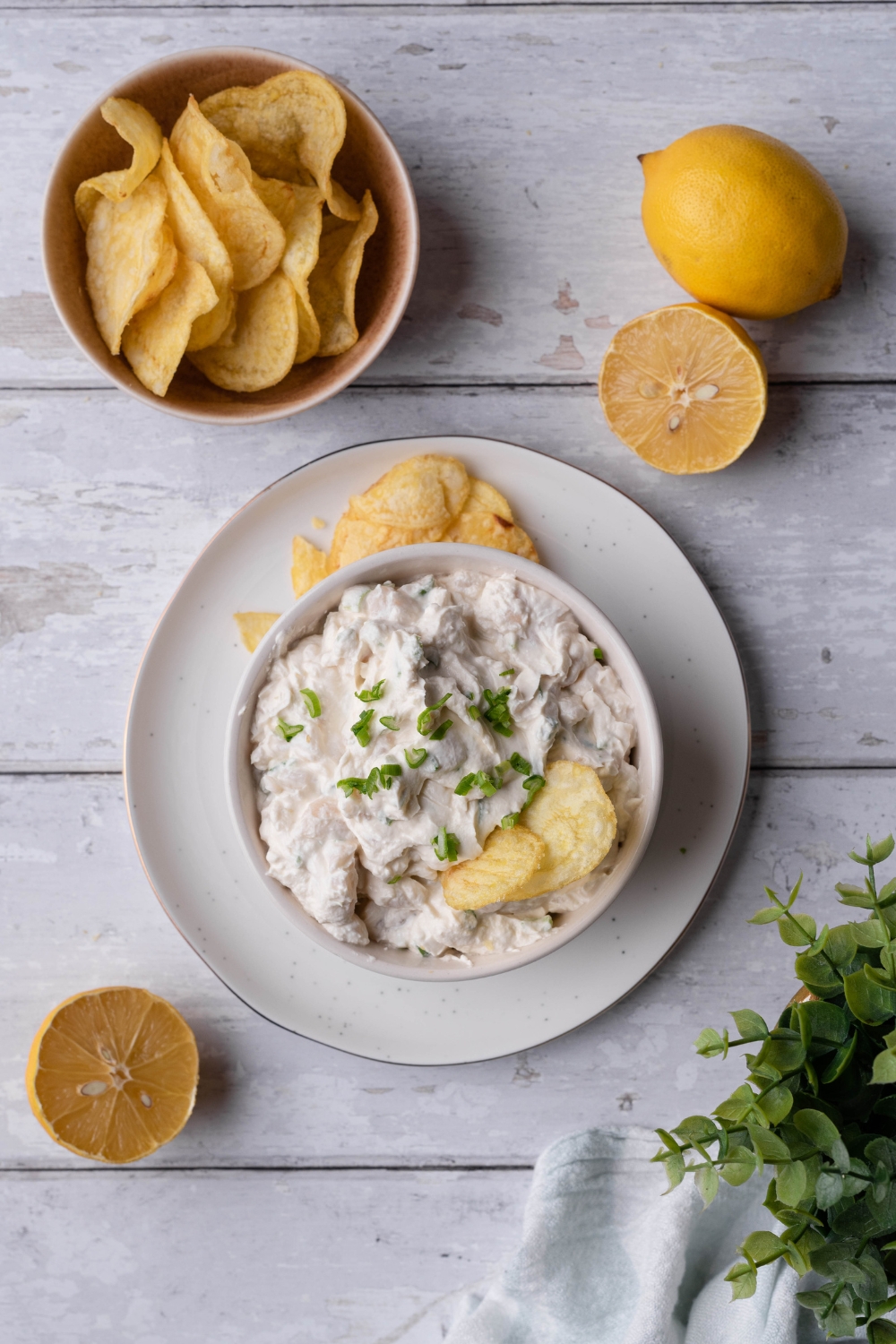 An overhead view of clam dip in a serving bowl on a plate with some potato chips on it. Another small bowl is next to the plate with potato chips in it.