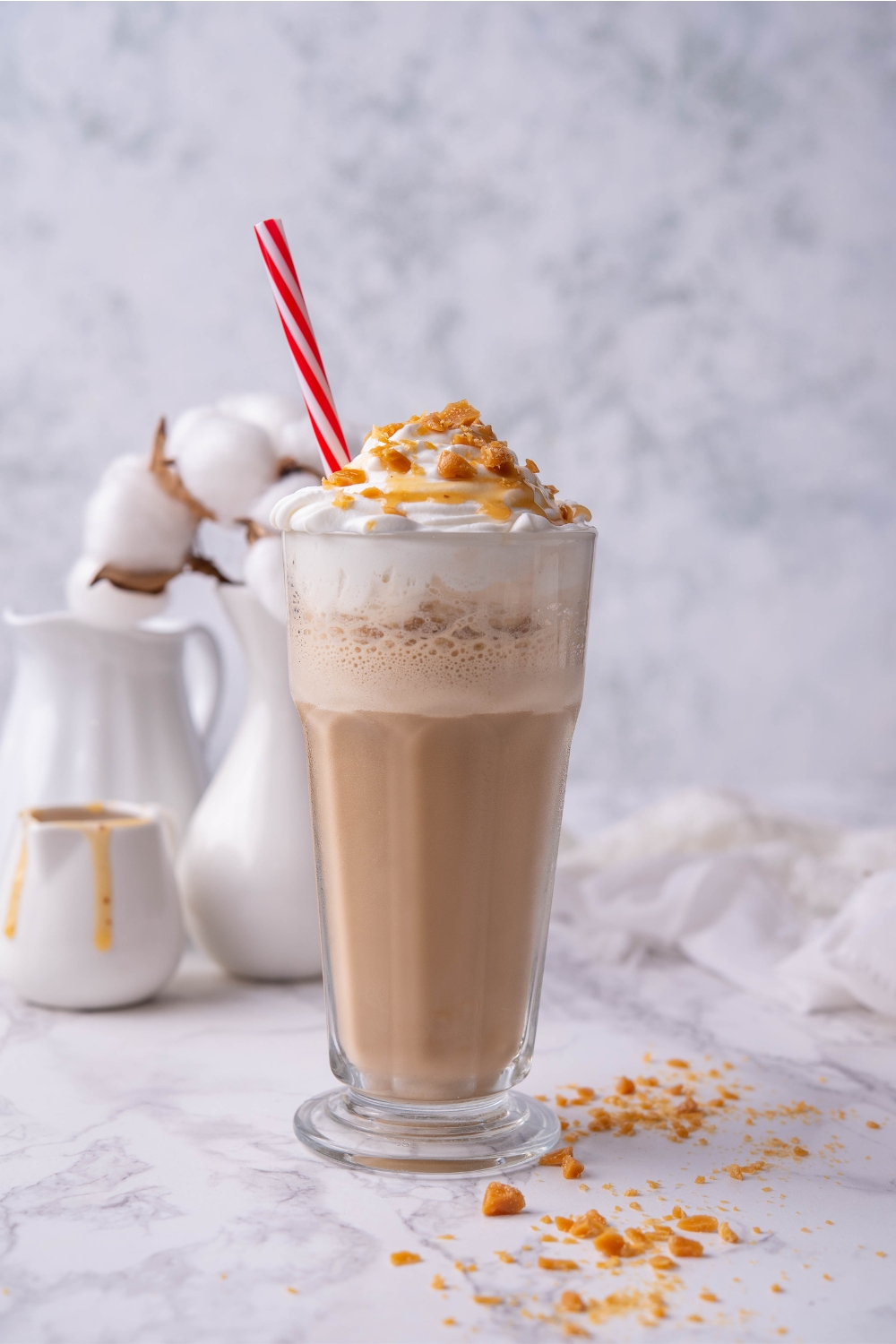 A tall glass with a caramel ribbon crunch frappuccino topped with whipped cream, caramel drizzle, and crunchy caramel topping.