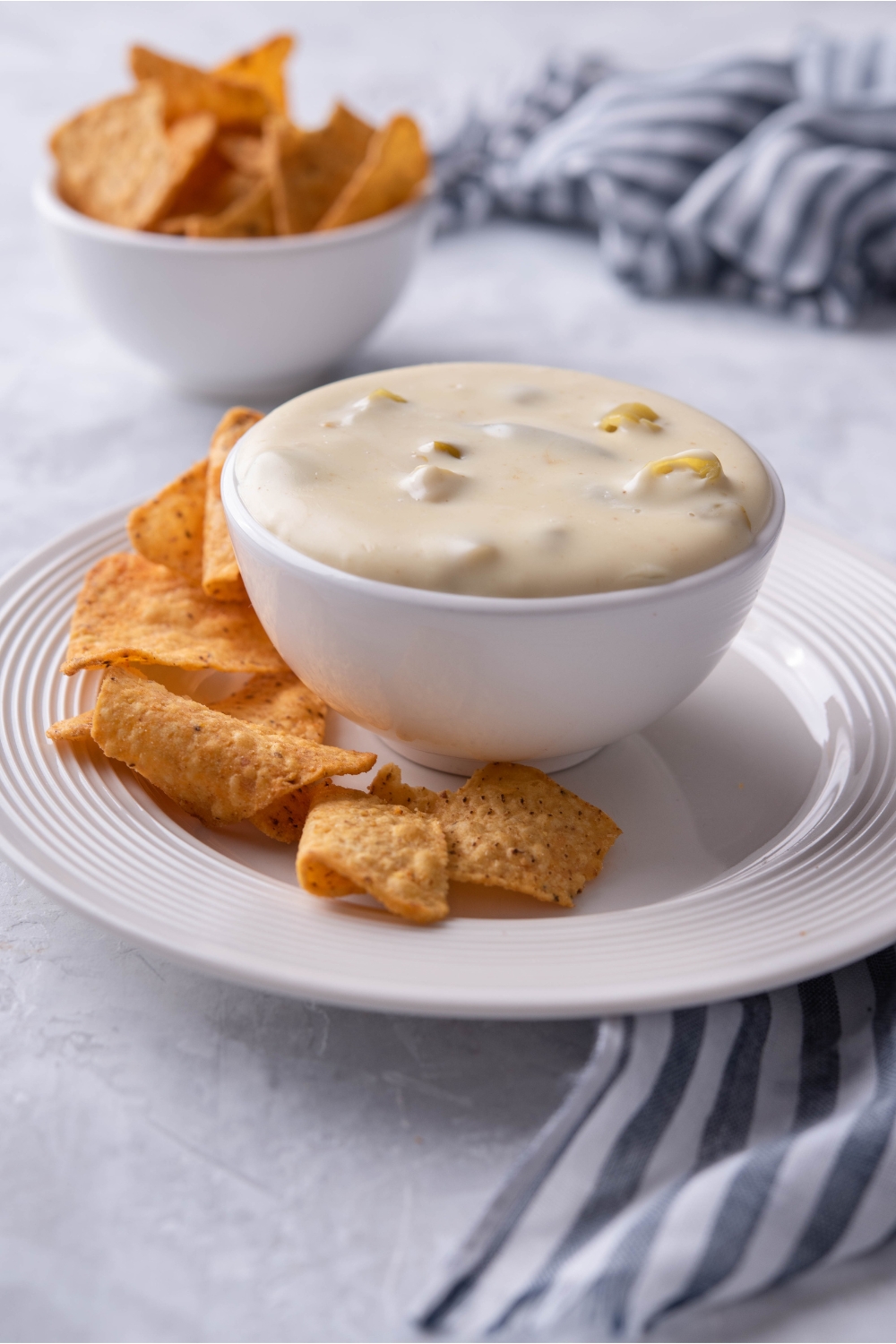 A small bowl with queso served on a plate with tortilla chips.