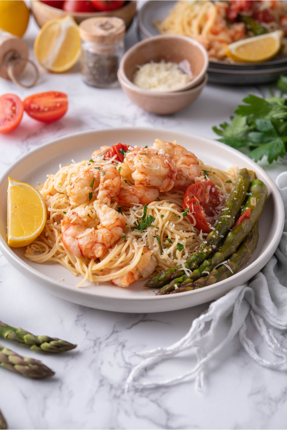 Olive Garden shrimp scampi piled on a white plate with a side of asparagus and a lemon wedge. The shrimp is garnished with fresh green herbs and there is a second serving of pasta in the background.