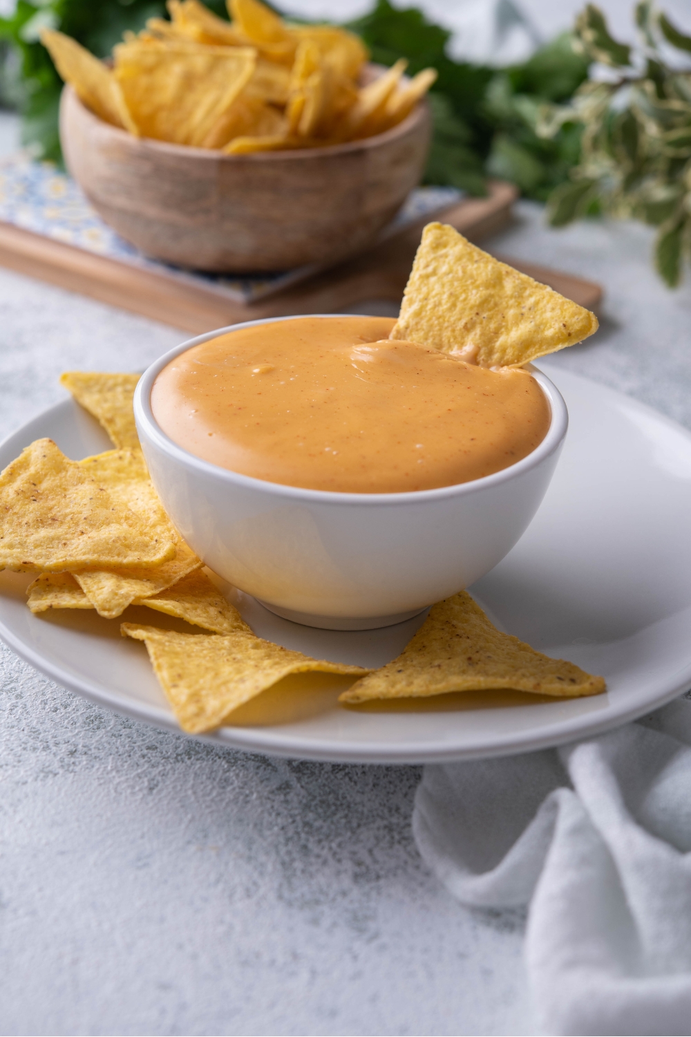 A tortilla chip sticking out of a bowl of Taco Bell nacho cheese sauce. The bowl is atop a plate filled with tortilla chips.