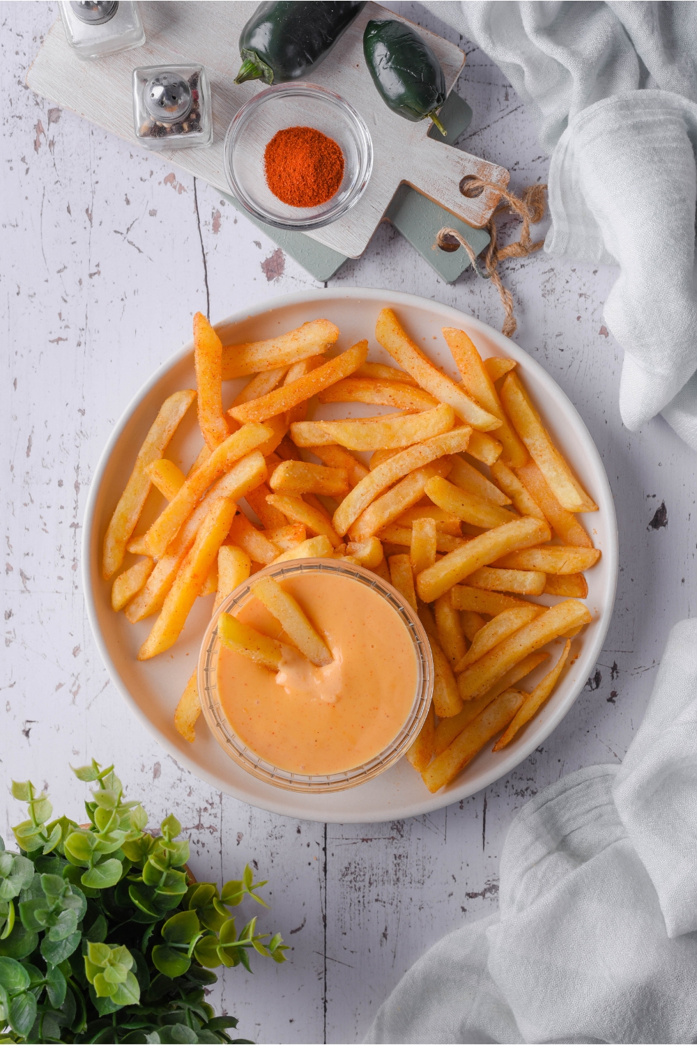 Overhead view of a plate of french fries with two fries stuck in the side dish of melted cheese sauce.