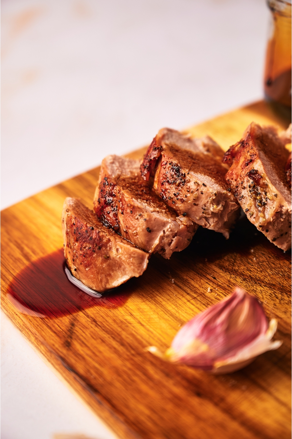 Close up of cooked pork tenderloin coated in a brown sauce atop a wood cutting board.