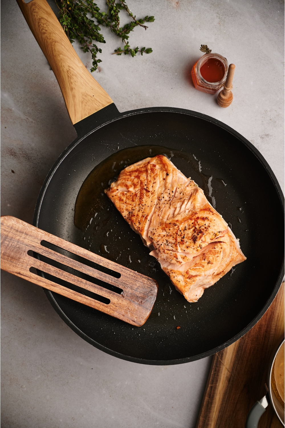 Salmon being seared in a black skillet with a metal spatula about to flip the salmon.
