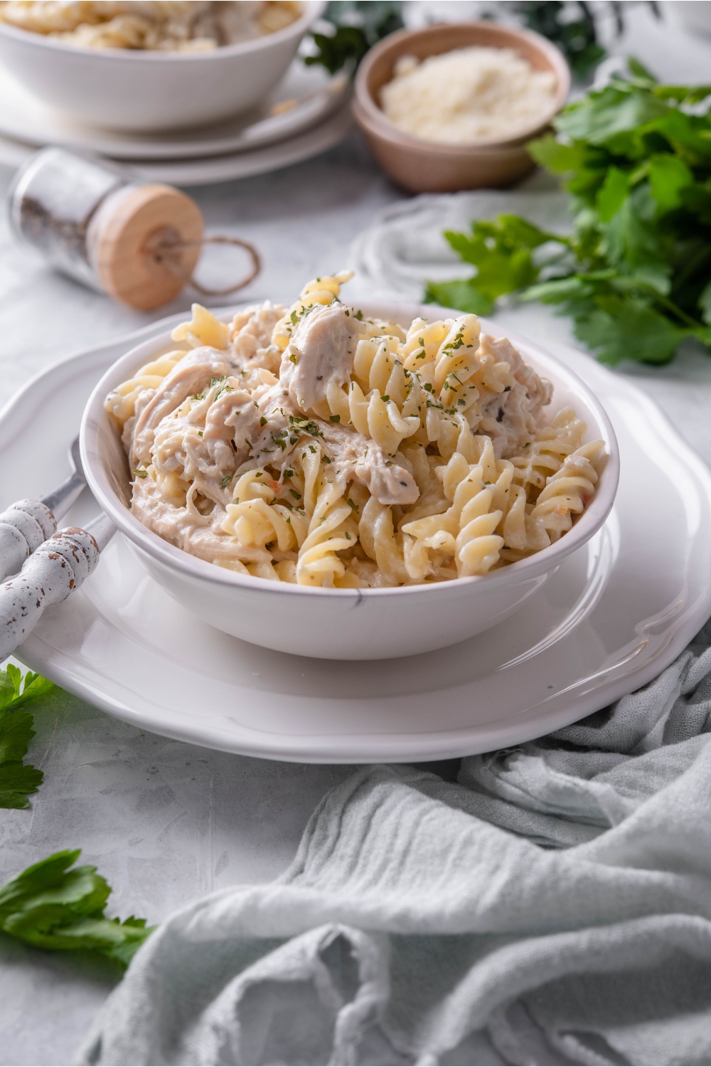 A bowl of pasta and chicken in a cream sauce atop a white plate with two forks next to the bowl.