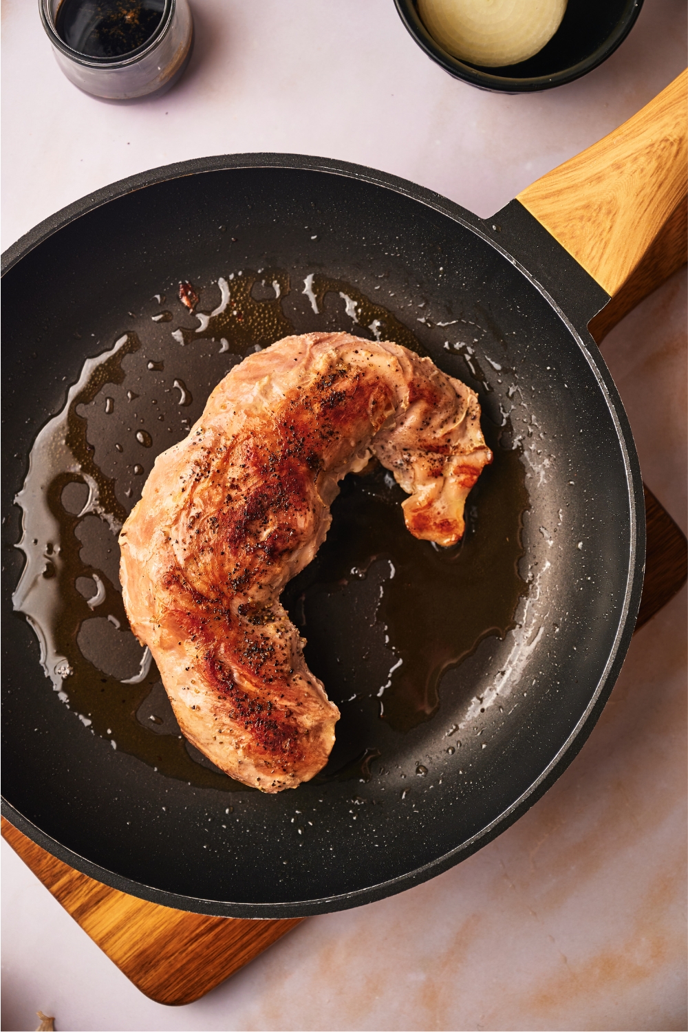 A cooked pork tenderloin being seared in a black skillet.