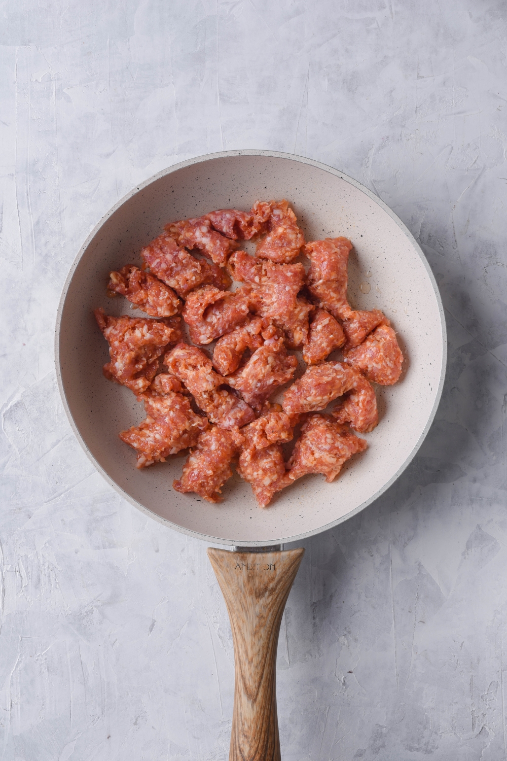 A grey skillet with uncooked sausage chunks in it.