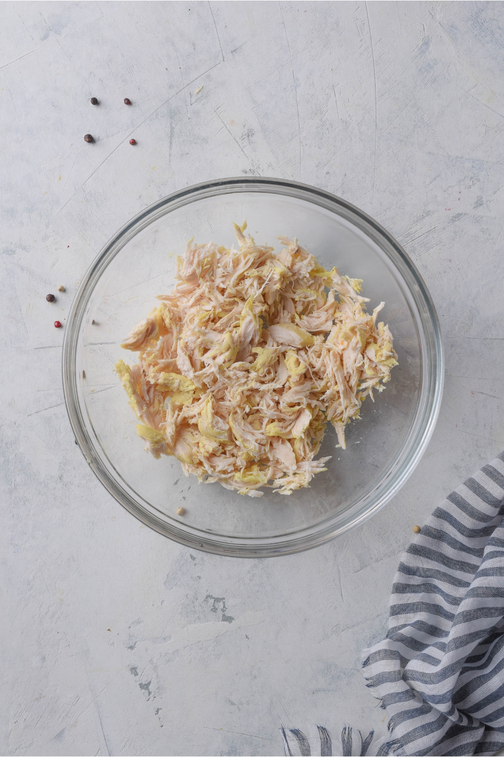 A clear bowl with shredded chicken and diced celery in it.