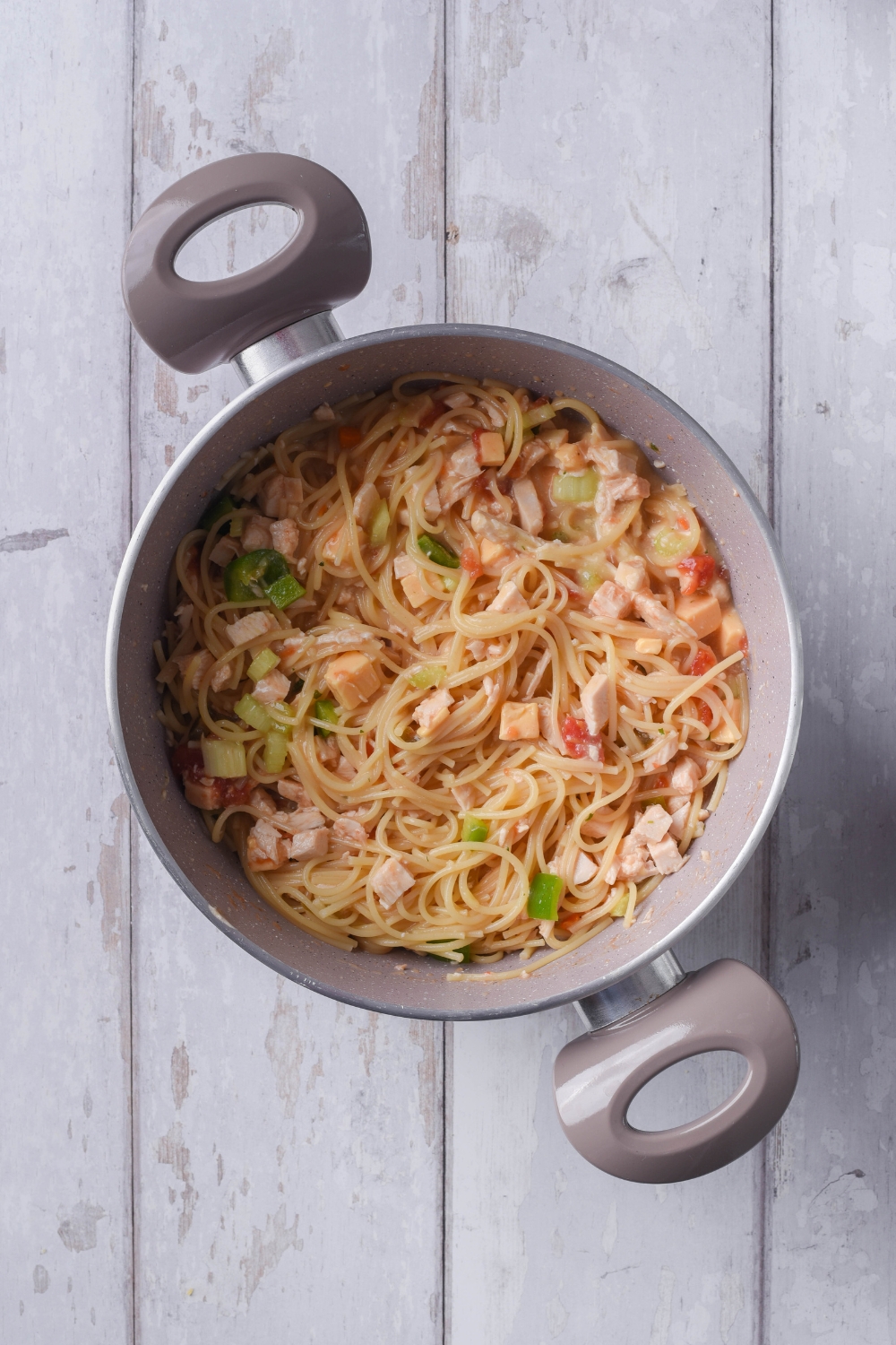 A large pot filled with spaghetti noodles, diced chicken, diced bell peppers, diced tomatoes, and diced celery.