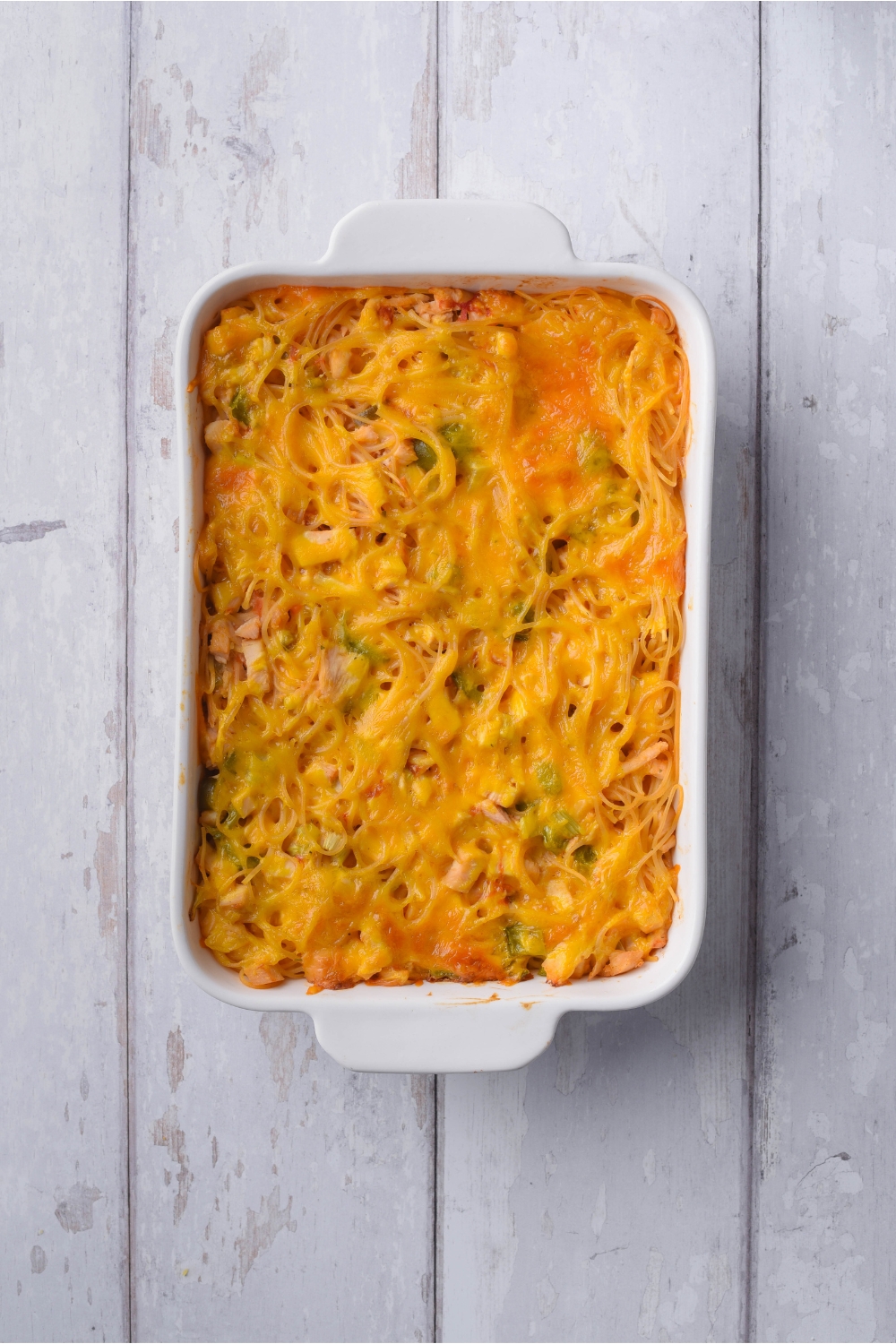 A baked chicken spaghetti casserole covered in melted cheese in a white baking dish.