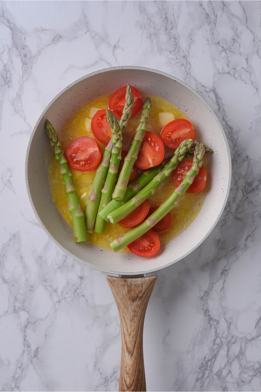 A grey skillet with melted butter, cherry tomatoes, and asparagus in it.
