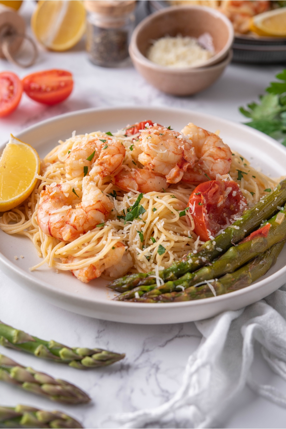 Olive Garden shrimp scampi piled on a white plate with a side of asparagus and a lemon wedge. The shrimp is garnished with fresh green herbs.