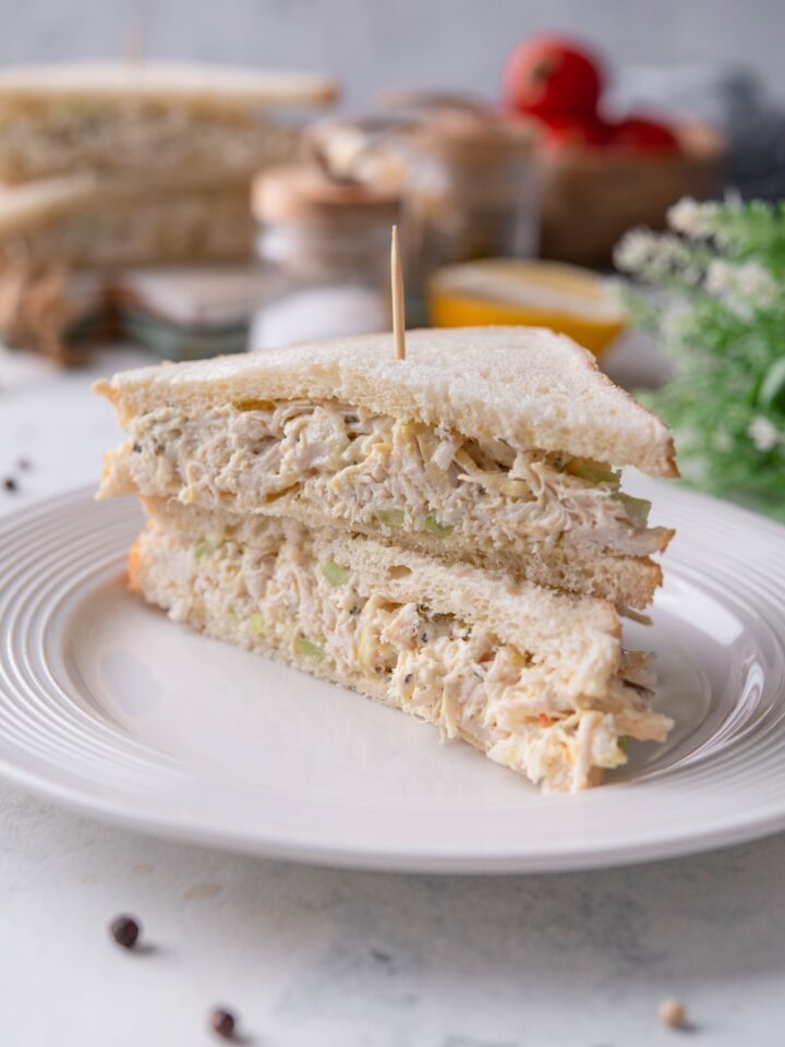 A chicken salad sandwich cut in half with both halves on top of each other and a toothpick running through them.