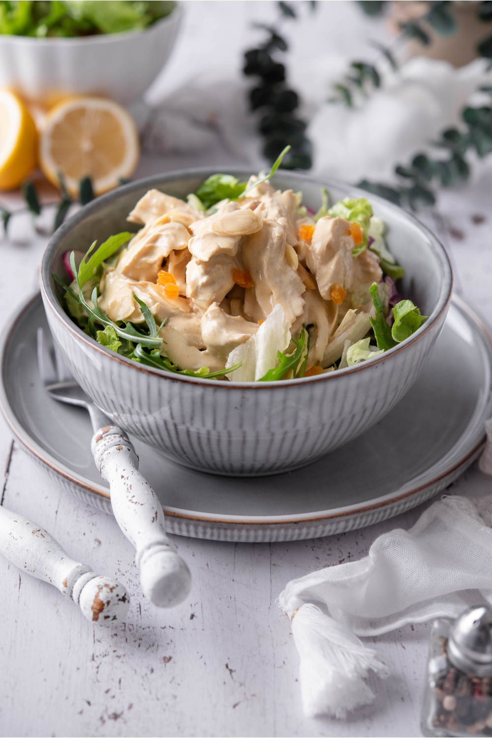 A blue bowl filled with coronation chicken salad atop a bed of greens. The bowl is on a blue plate and there is a fork on the plate.