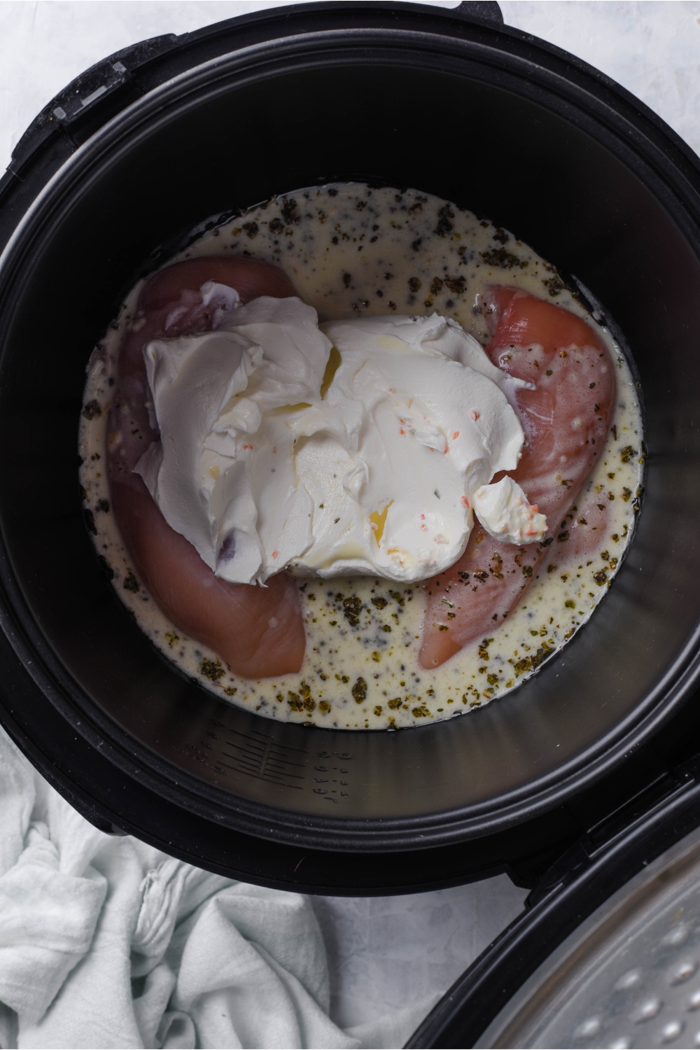 A slow cooker filled with raw chicken, creamy dressing, and cream cheese in it.