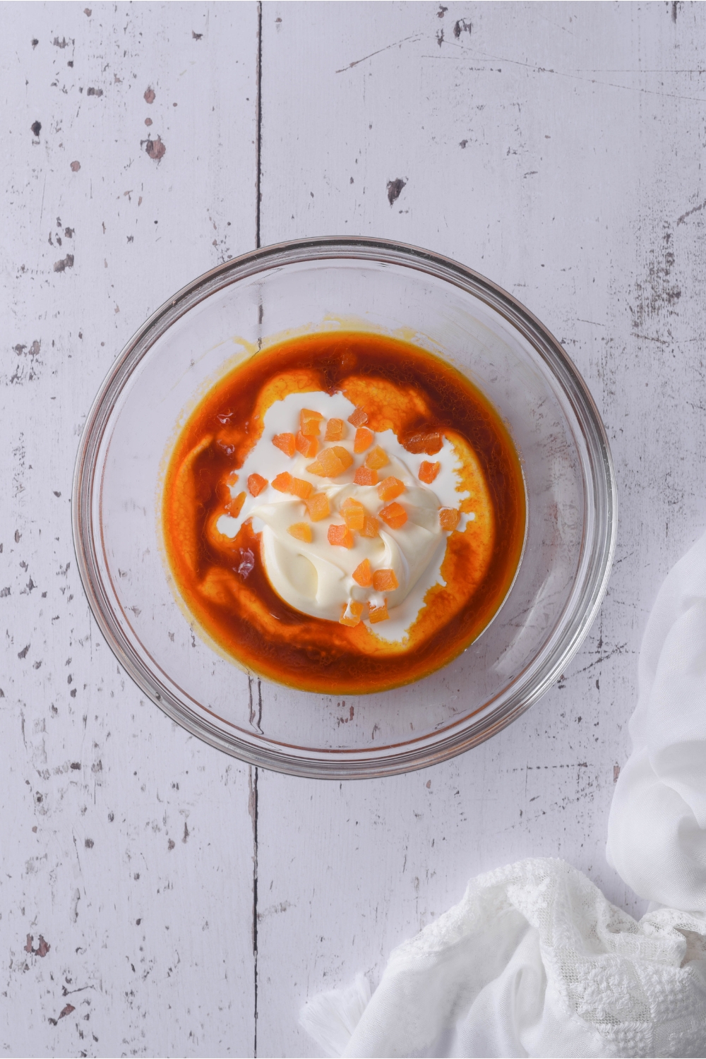 A clear bowl with mayonnaise, creme fraiche, a red sauce mixture, and diced apricots. The ingredients have not yet been mixed together.