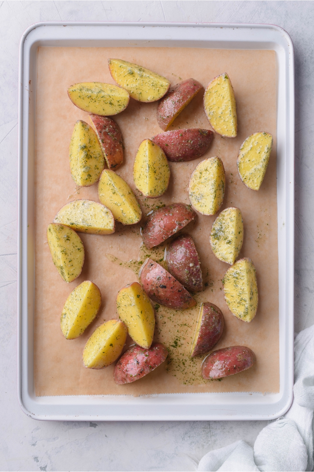 Quartered and seasoned potatoes seasoned with oil and ranch seasoning spread out evenly on a baking sheet lined with parchment paper.
