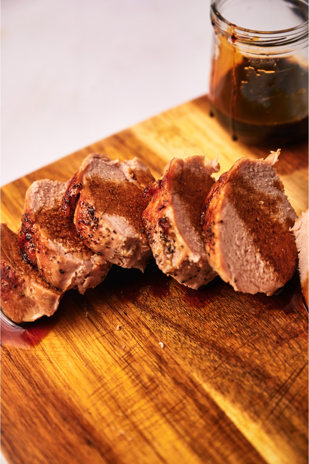 Close up of cooked pork tenderloin coated in a brown sauce atop a wood cutting board.